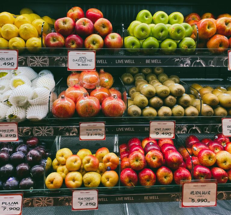 assortment of fruits displayed with prices on grocery store shelves